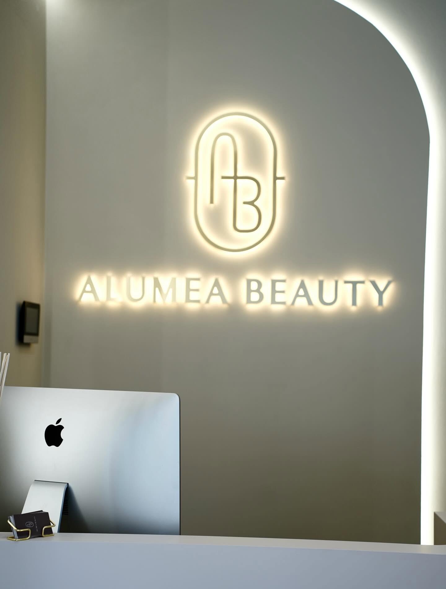 Podświetlony monogram AB i napis Alumea Beauty nad recepcją